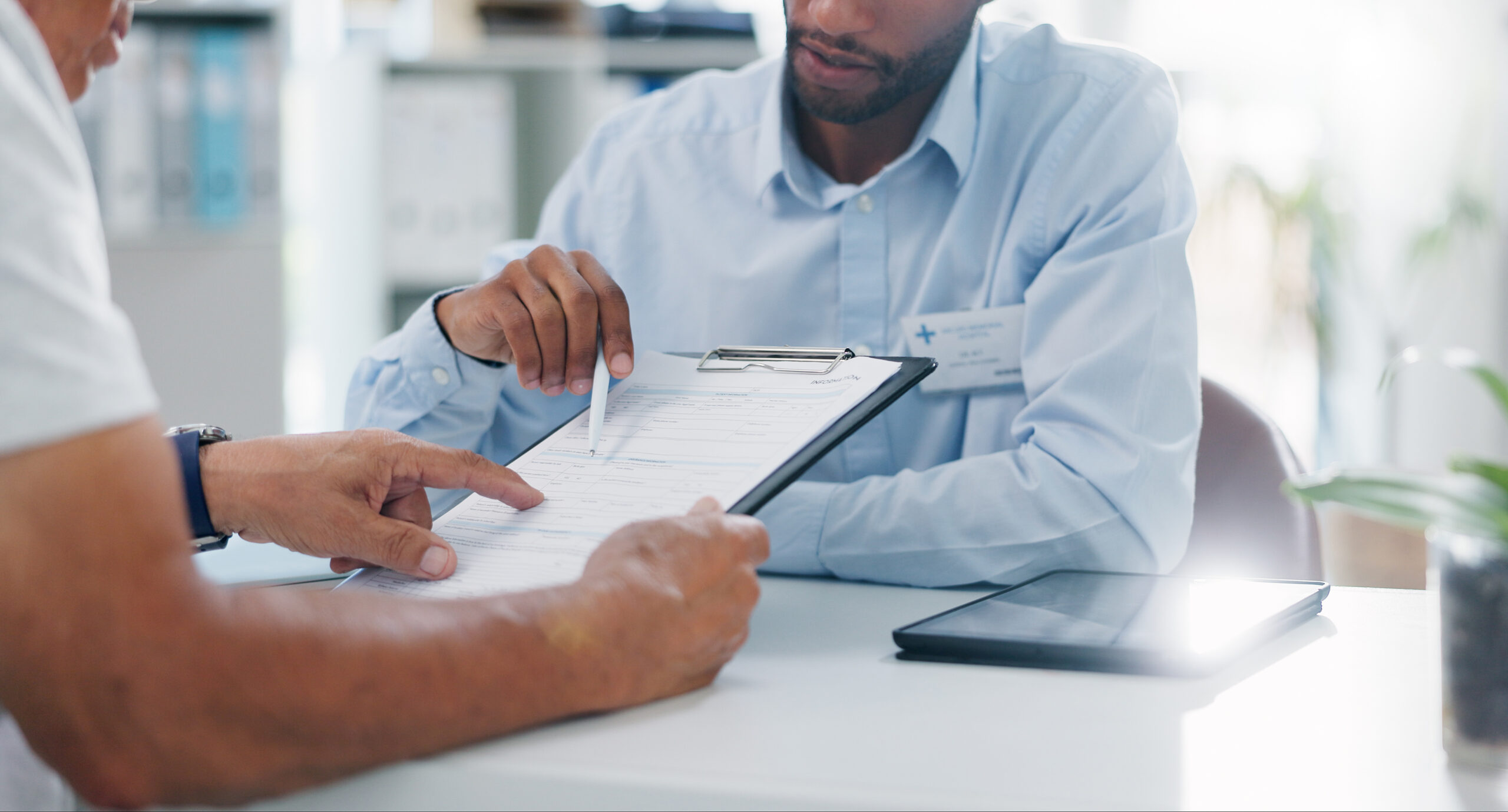 Two people review and discuss a form on a clipboard at a desk in a professional office setting, exploring Medicaid options for housing providers.