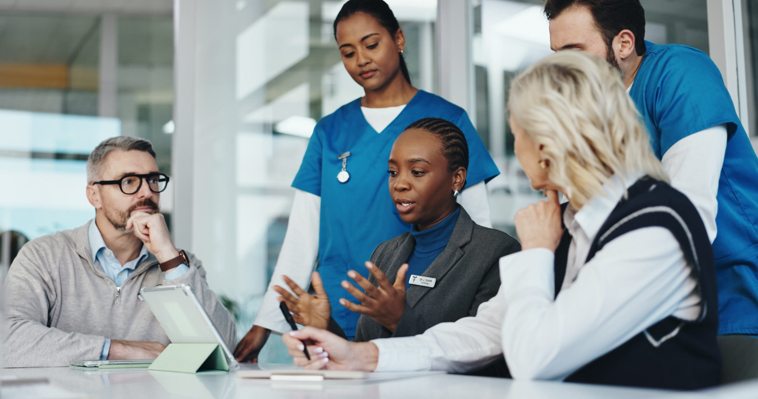 A diverse group of professionals, including healthcare workers, discuss ideas around a table in an office, focusing on Affordable Housing and Medicaid Provisions to better serve their community.