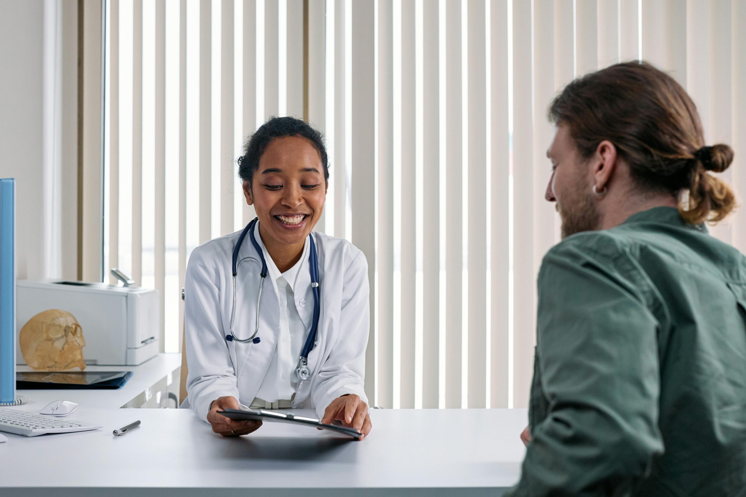 A smiling doctor shows a tablet to a patient during a consultation in a bright office, discussing health care coverage options and eligibility checks.
