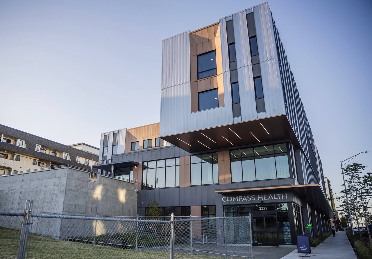 Modern Compass Health building with large windows, metal panels, and a fenced area in front under a clear sky—reflecting a commitment to investing in quality healthcare spaces.