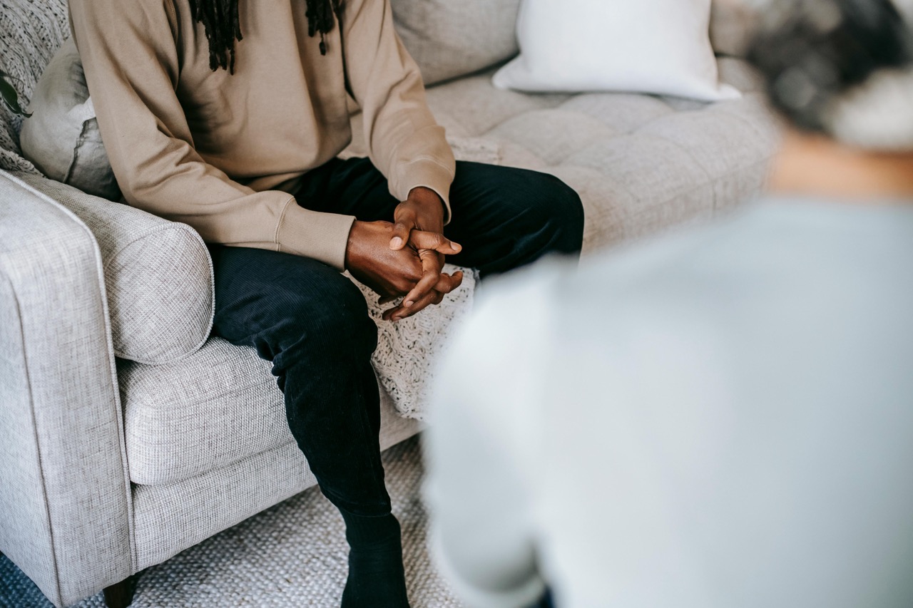 Person sitting on a light-colored couch with hands clasped, engaged in conversation at the Center for Innovations, talking to someone out of focus in the foreground.