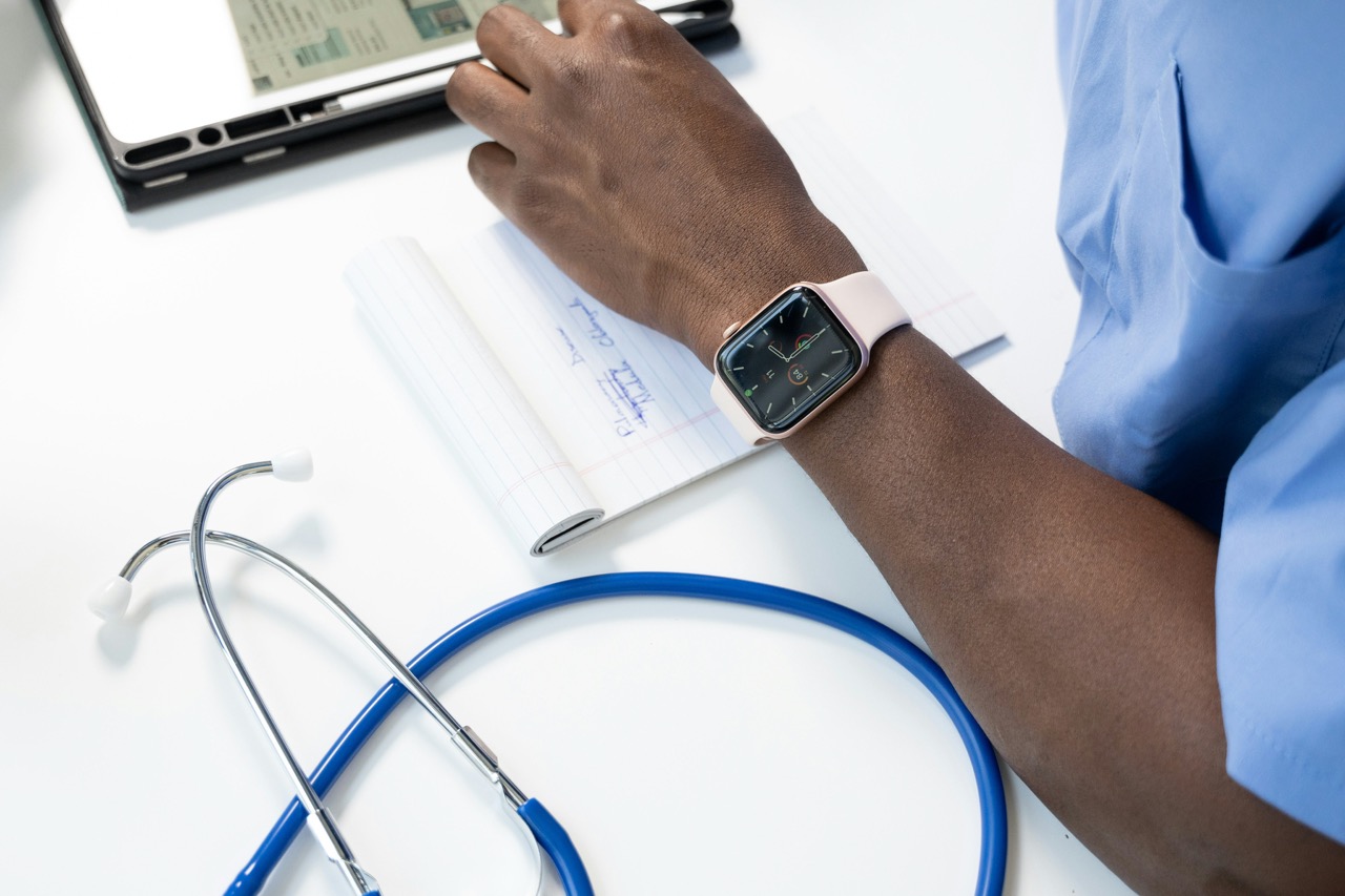 Person in scrubs writing notes at a desk with a stethoscope, tablet, and smartwatch visible, considering policy solutions to improve healthcare practices.