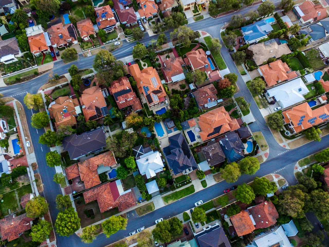 Aerial view of a suburban neighborhood with houses, streets, trees, and parked cars—an inviting scene for investing or lending in real estate opportunities.