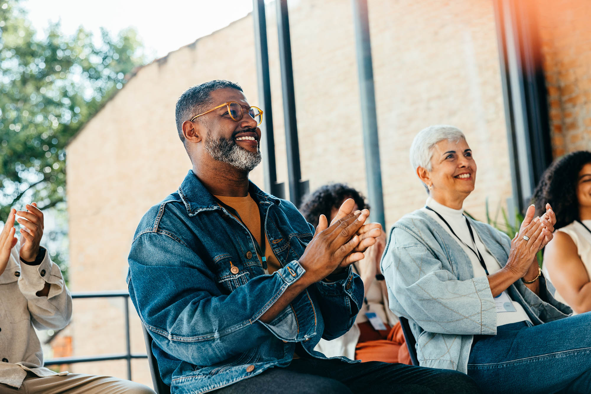 A group of adults sitting and clapping, appearing to attend an event or presentation at the National Center for Housing & Health in a bright, indoor setting with large windows.