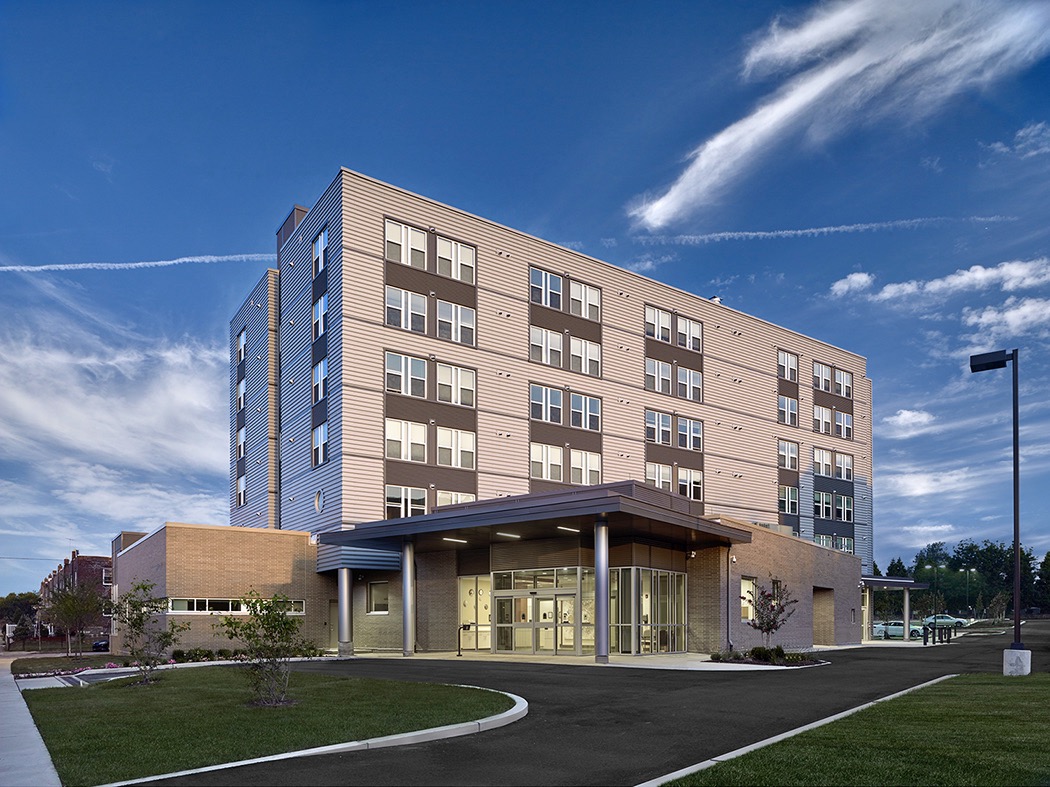 Modern five-story building with large windows under a blue sky, surrounded by grass and a paved driveway—ideal for investing or lending opportunities in growing urban areas.
