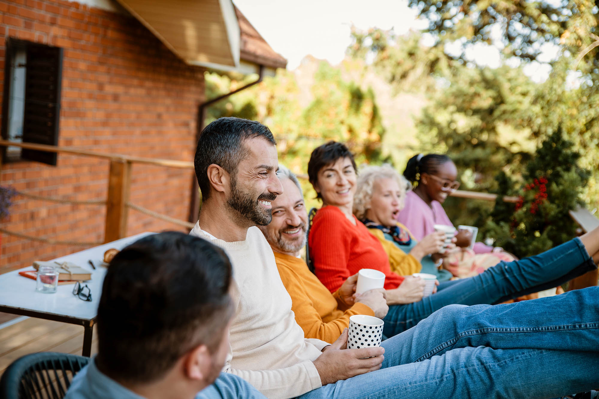 A group of friends sit outdoors on a porch at the Center, smiling and chatting about recent innovations while holding cups.