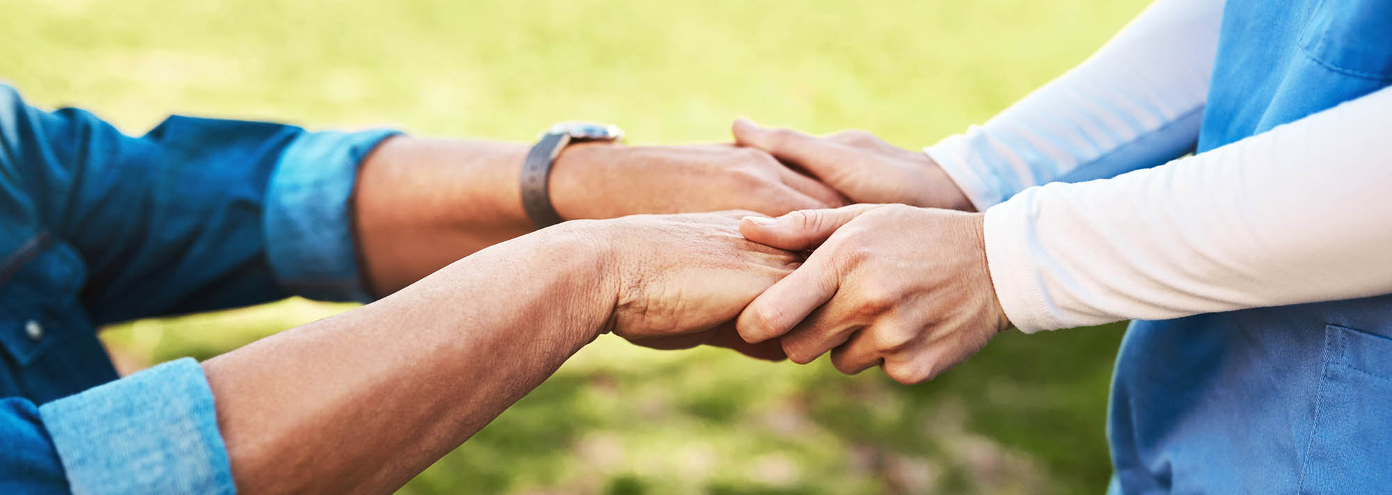 A caregiver gently holding an older adult’s hands outdoors, showing support, compassion, and connecting them to relevant resources for their well-being.