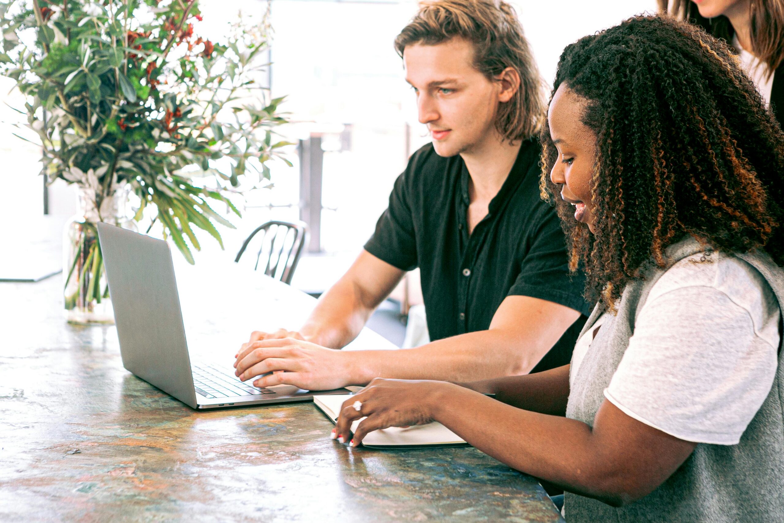 Two people working together at a table, one using a laptop to analyze data while the other takes data-driven notes in a notebook, both focused on making an impact.