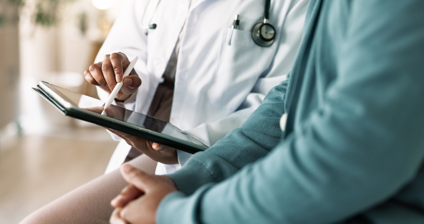 Doctor using a digital tablet with a patient sitting nearby, both focused on the screen.