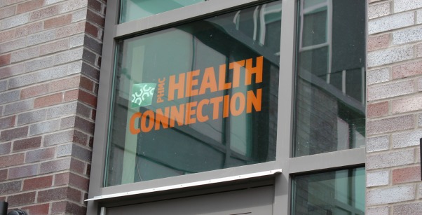 A glass door with PHMC Health Connection in orange letters on a brick building.