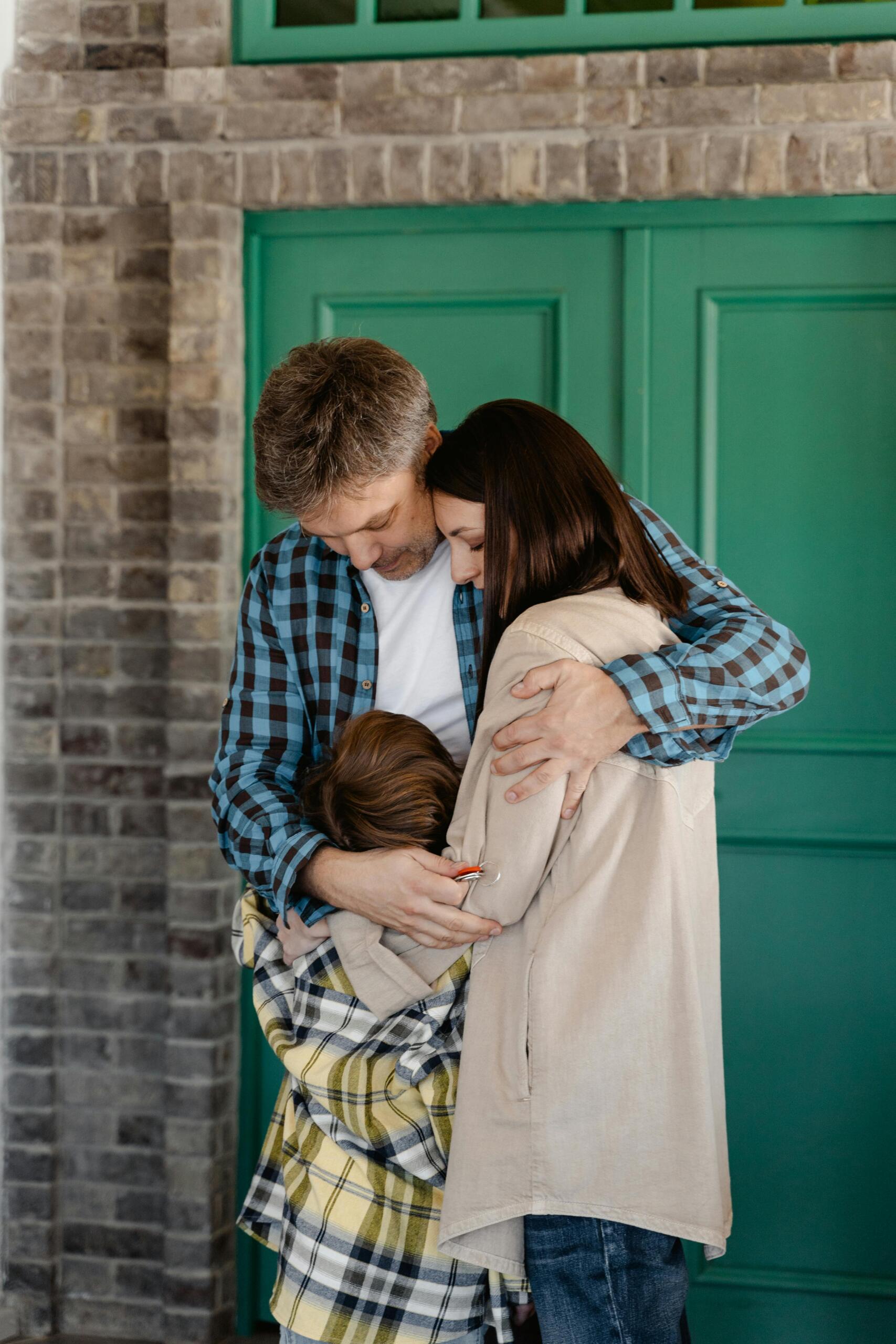 A man, woman, and child stand in front of a green door, hugging each other closely—evidence of the warmth and security found in supportive housing.