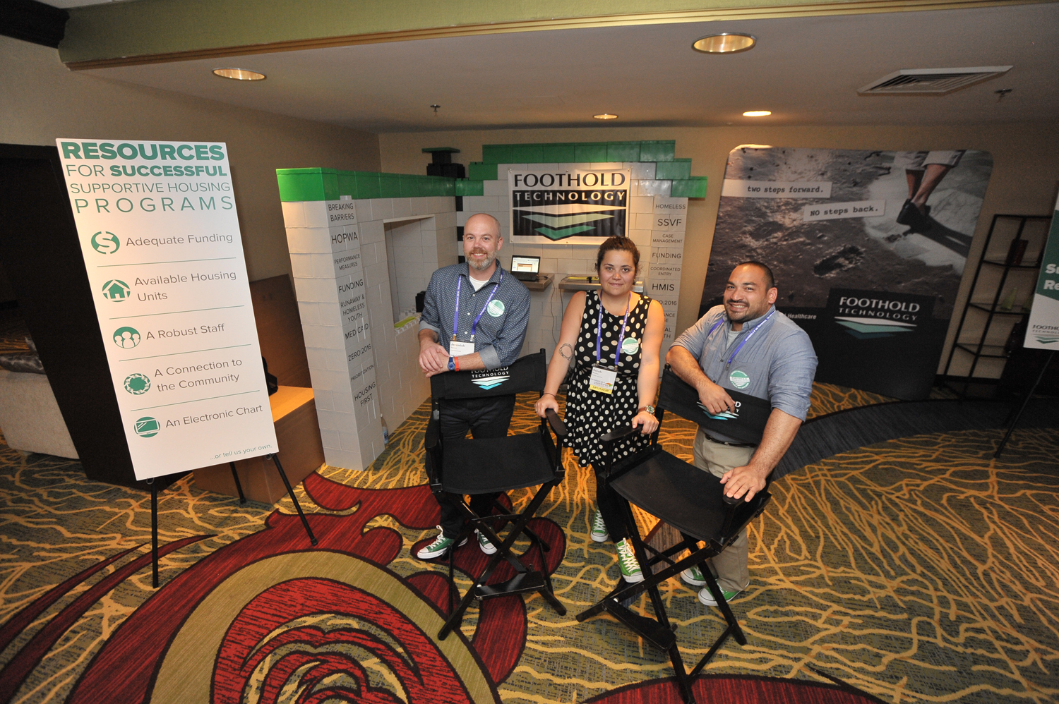Three people at a Foothold Technology booth with a sign about supportive housing program resources.
