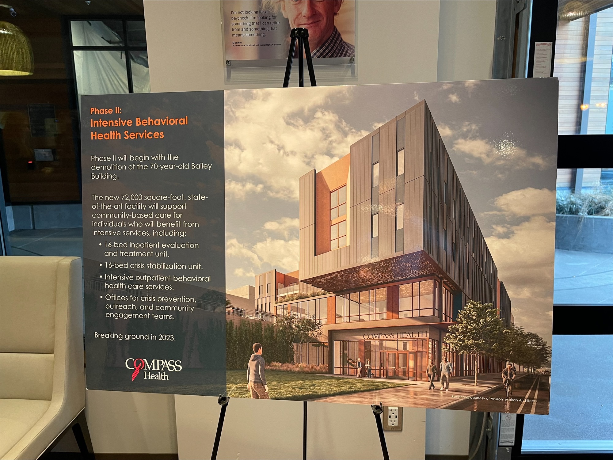 Poster on an easel shows a modern building rendering and details about Compass Health’s new behavioral health facility.